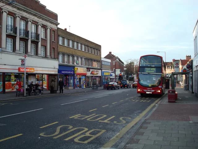 A red double-decker bus at a stop on Sidcup High Street, with shops along the pavement and BUS STOP painted on the road