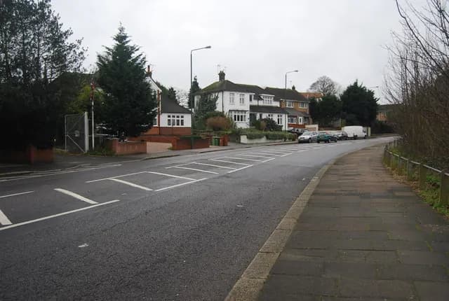 Woolwich Road in Belvedere, a wide road with white hatched markings, houses behind hedges and a footpath beside it